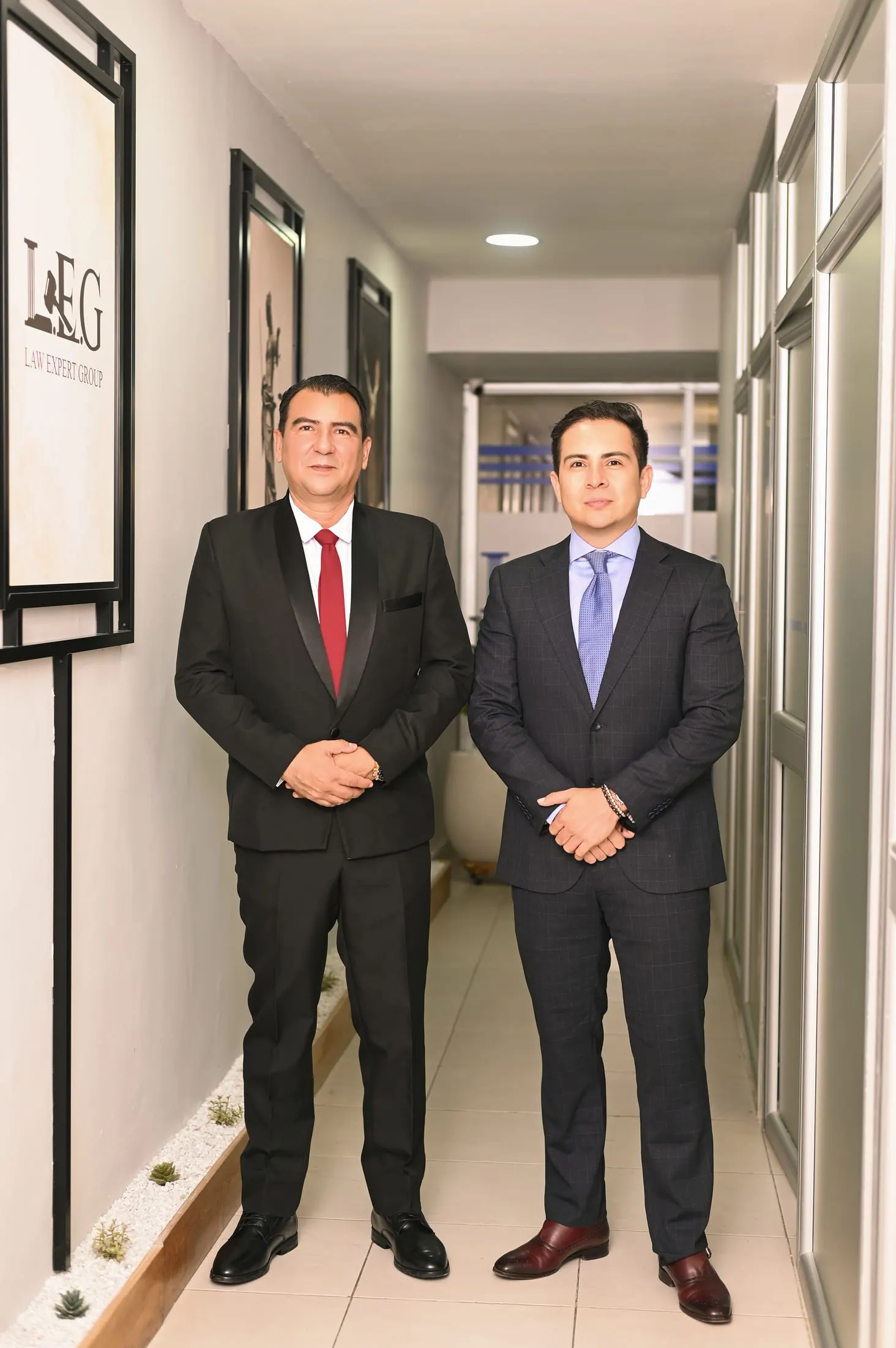 Eduard A. Vásquez Sierra y Antonio Camargo Paternina, de pie en un pasillo de las instalaciones de la firma, junto a su logotipo